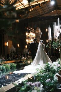 Wedding guests enter an indoor ceremony space while umbrellas and wet coats are placed near the doorway.